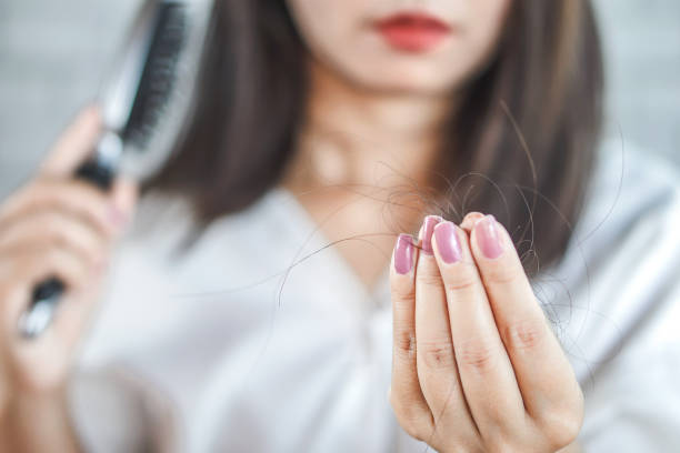 image6 Close-up of a woman examining loose hair strands held between her fingers, with a hairbrush in the blurred background.