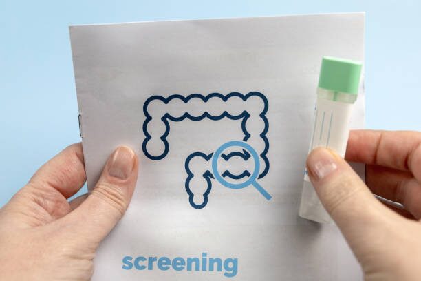 Hands hold a page showing a blue outlined large intestine with a magnifying glass over a section, symbolizing colorectal screening.