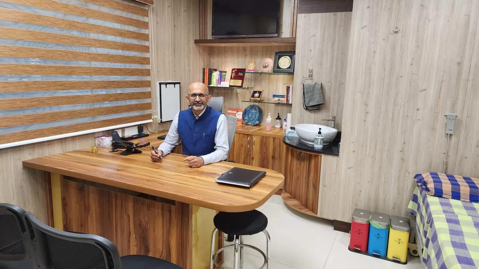 image5 Man seated at a curved wood reception desk in a bright office, pen in hand and a binder on the desk.