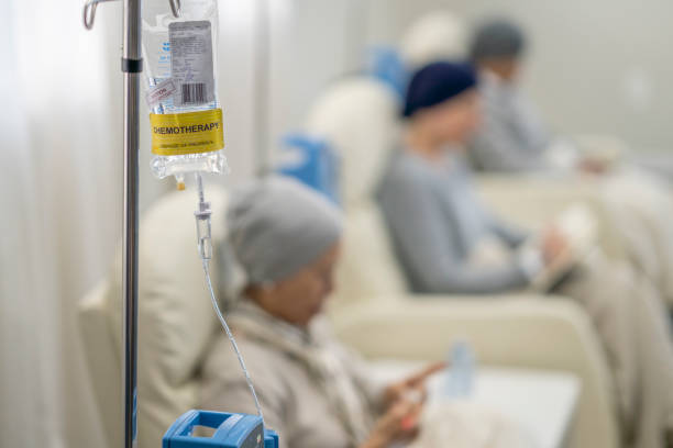 image8 IV chemotherapy infusion bag hangs from a pole in a hospital lounge, with blurred patients seated in the background.